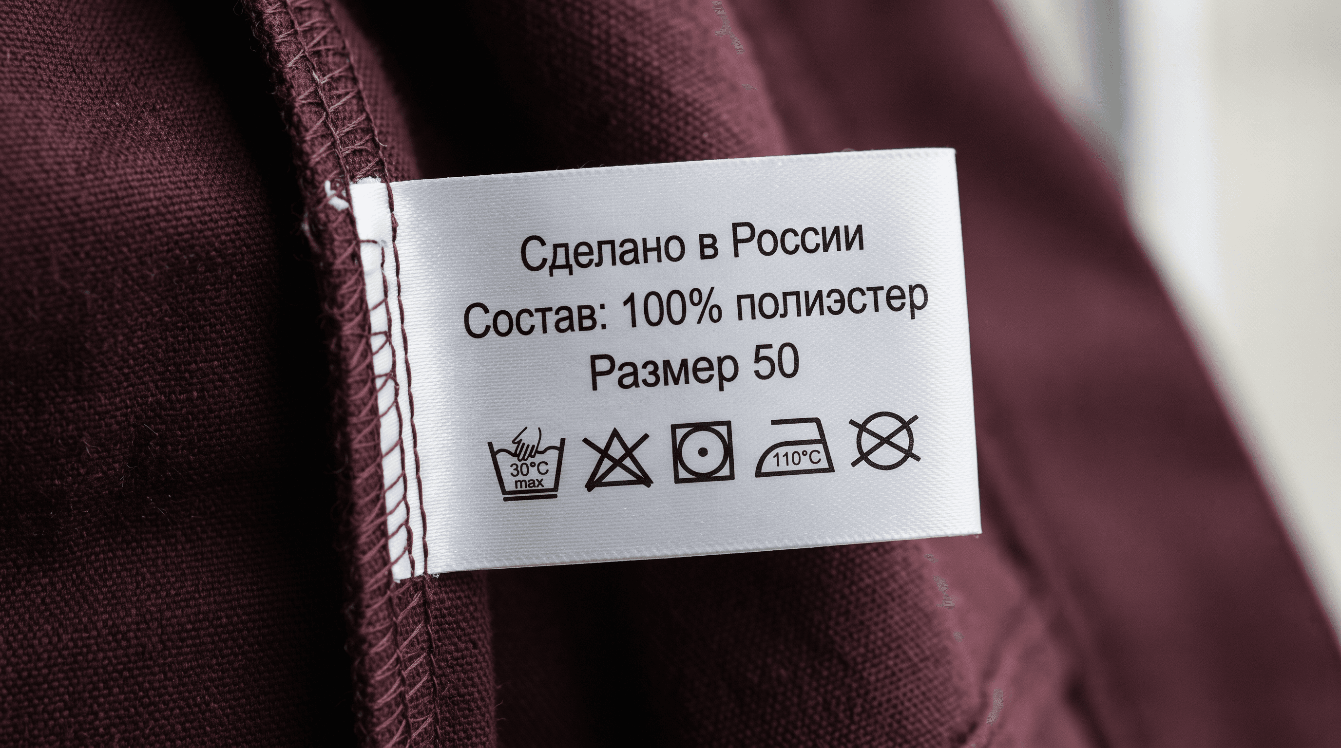 Белая полиэстеровая бирка с составом и знаками ухода, вшитая в шов рабочей куртки