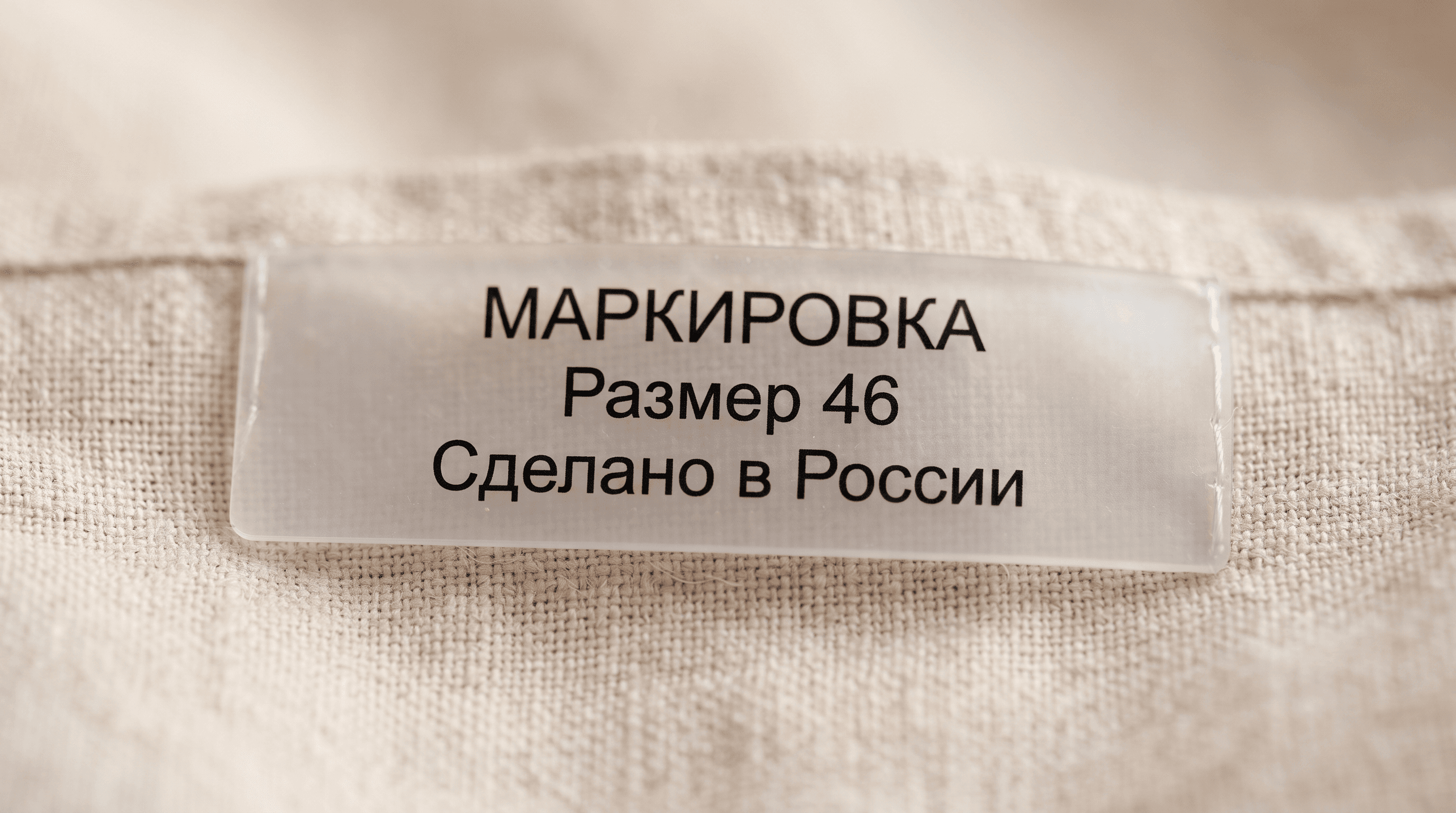Плоская прозрачная силиконовая бирка с чёрным русским текстом «МАРКИРОВКА, Размер 46, Сделано в России» на светлой ткани изделия